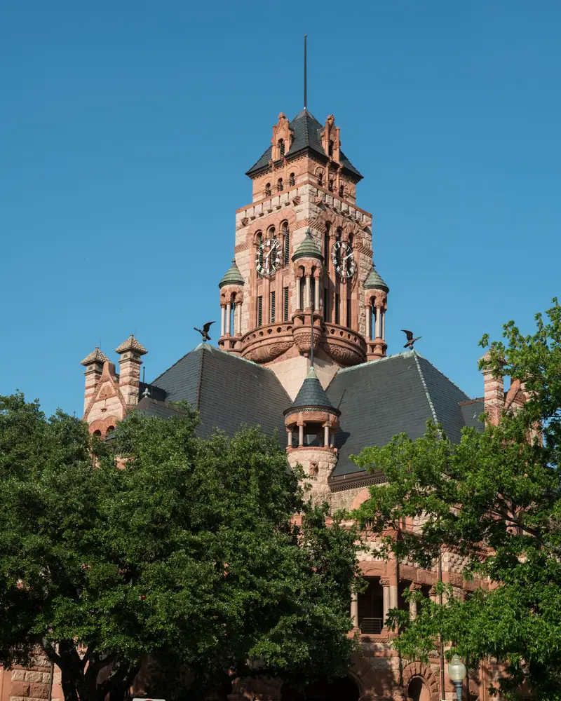 The red granite clock tower of the 1897 Ellis County Courthouse in downtown Waxahachie, against a blue sky